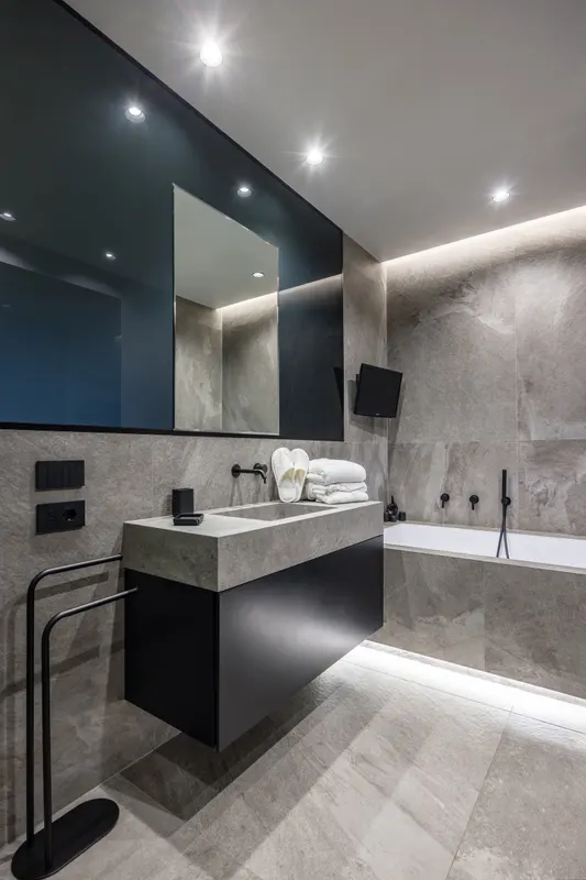Bagno en suite di Santopaolo 2 in pietra grigia, lavabo, vasca e TV